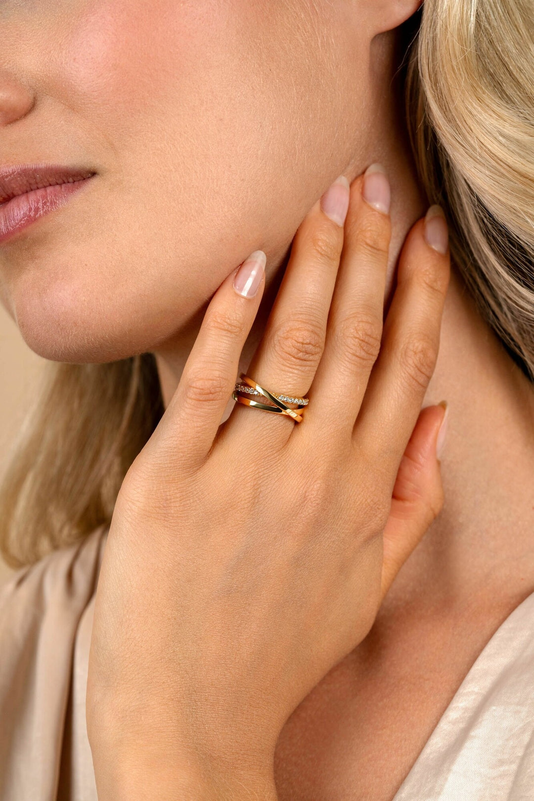 Een close-up van een vrouw met een lichte huid en blond haar die haar wang aanraakt, gemanicuurde nagels toont en de Zinzi Ring Gold Plated ZIR1774Y van Zinzi om haar vinger draagt.