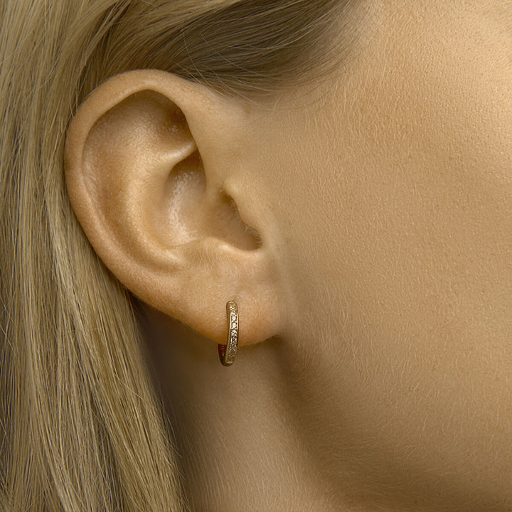 Close-up van het oor van een vrouw versierd met Van der Kooij Collectie klapoorringen zirkonia, geaccentueerd met fonkelende steentjes. Haar blonde haar en lichte huid benadrukken de verfijnde elegantie van deze gouden oorbellen.