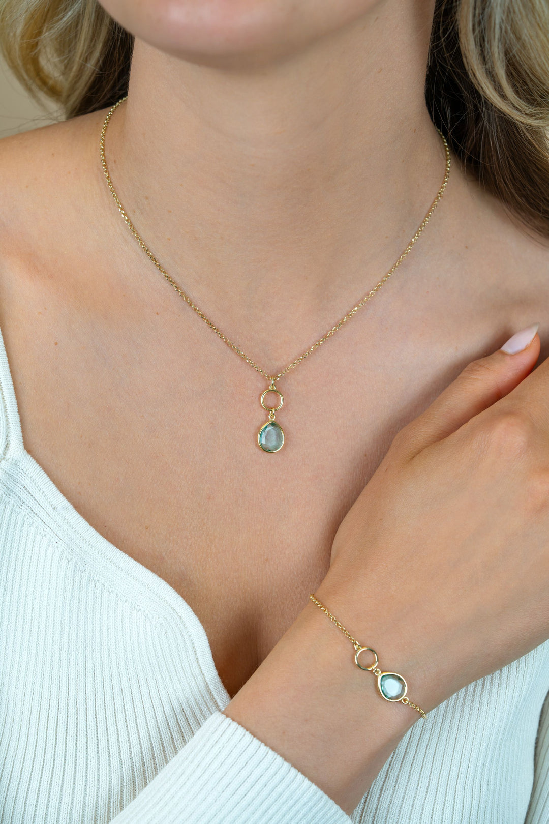 Een vrouw draagt de Zinzi ketting verguld ZIC2716G met een ronde turquoise hanger van Zinzi en een bijpassende gouden armband met een aqua edelsteen. Haar nagels zijn gemanicuurd en ze draagt een wit topje.