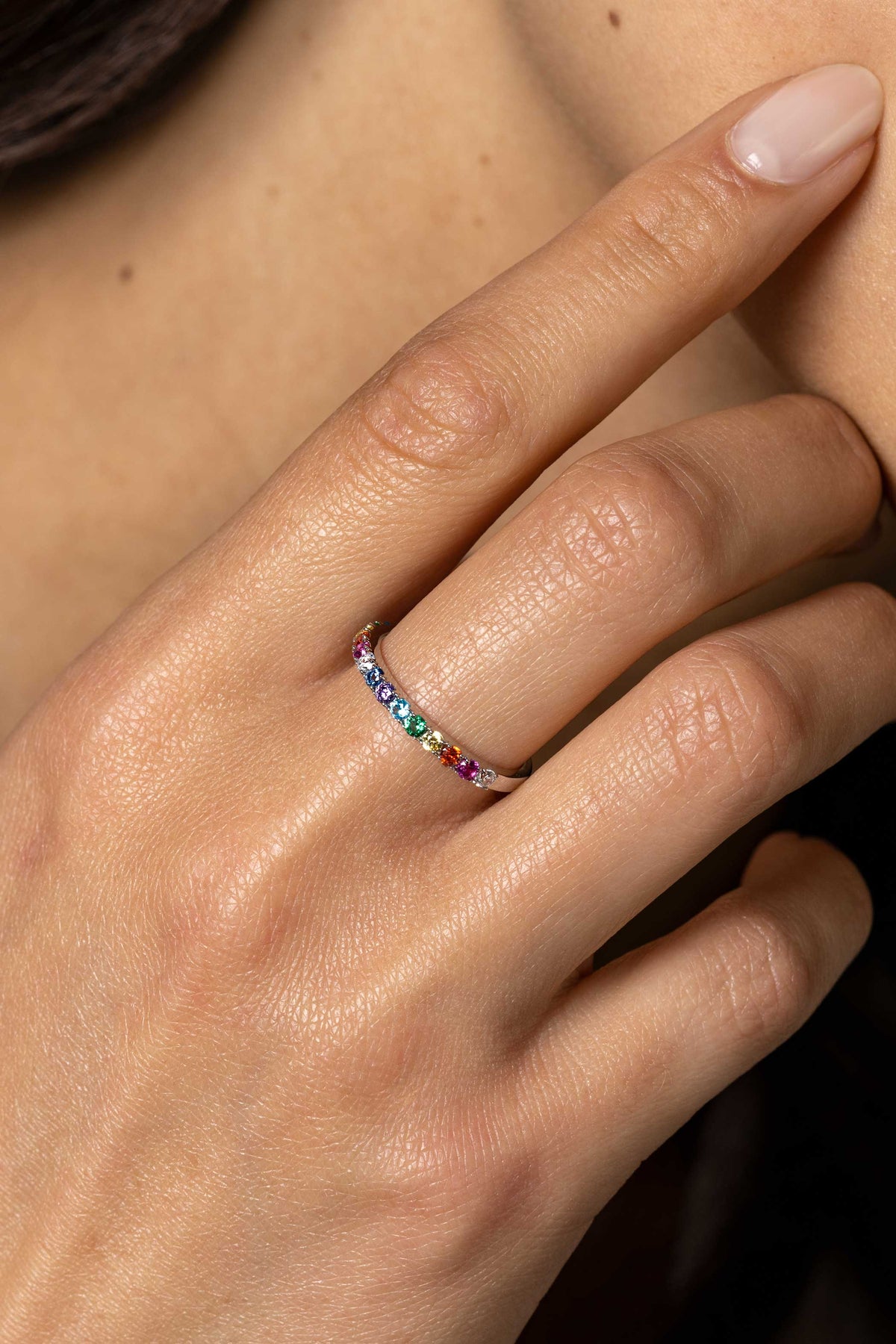 Een close-up van een hand met een nude manicure, die de Zinzi Ring Zilver Zir2486 bezet met kleine regenboogkleurige steentjes draagt en zachtjes de kin aanraakt.