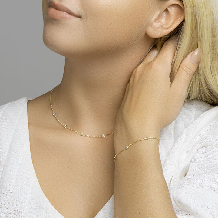 Een vrouw in een witte top met V-hals strijkt zachtjes over haar hals, draagt een gouden halsketting en de Van der Kooij Collectie armband zirkonia 17 + 2 cm 3 micron zilver verguld (geel)- het perfecte accessoire voor stijlvolle dames.