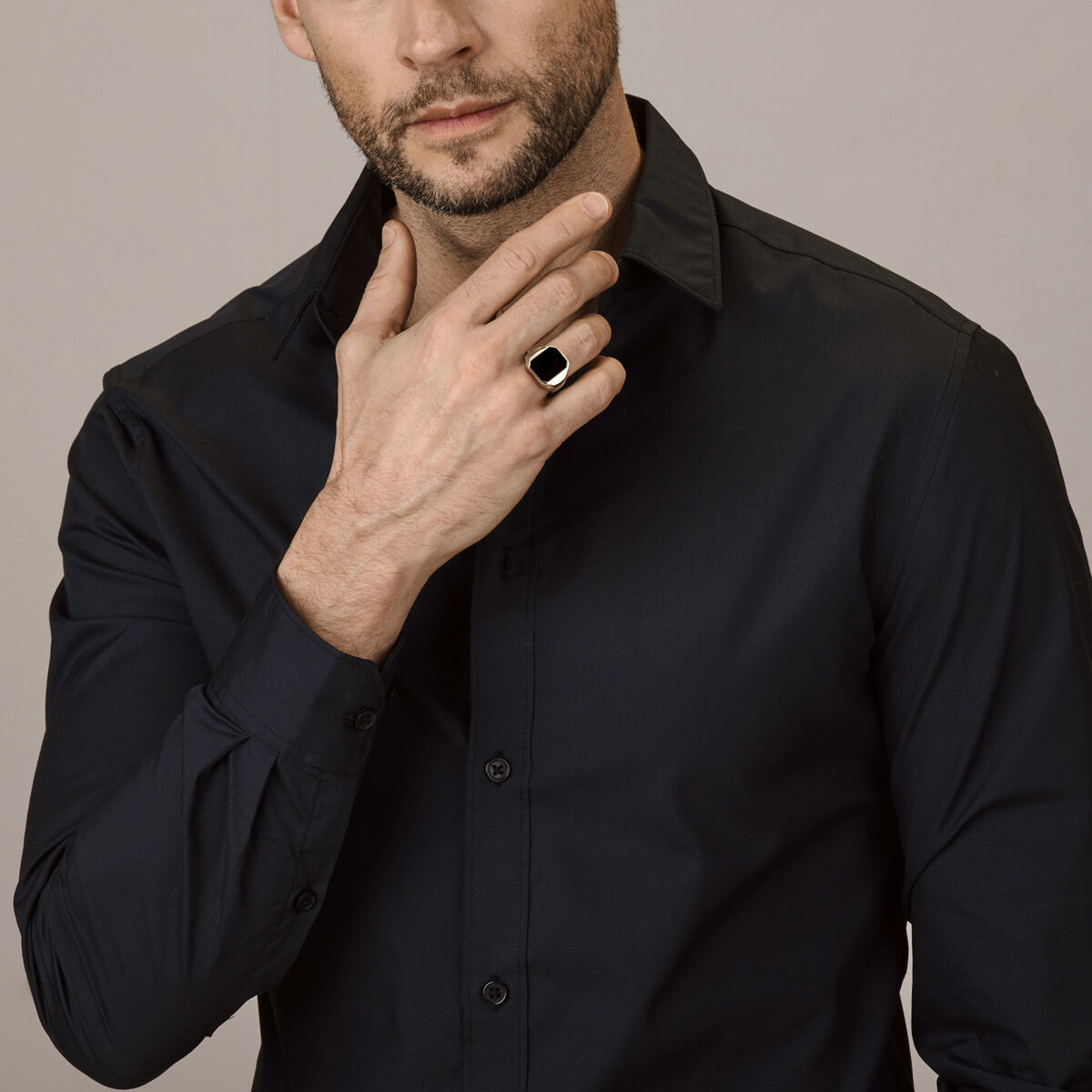 Een man in een donker overhemd raakt zijn kin aan en toont de Van der Kooij Collectie zegelring onyx 14K geelgoud – een opvallende rechthoekige ring van zwarte onyx – tegen een effen lichte achtergrond.