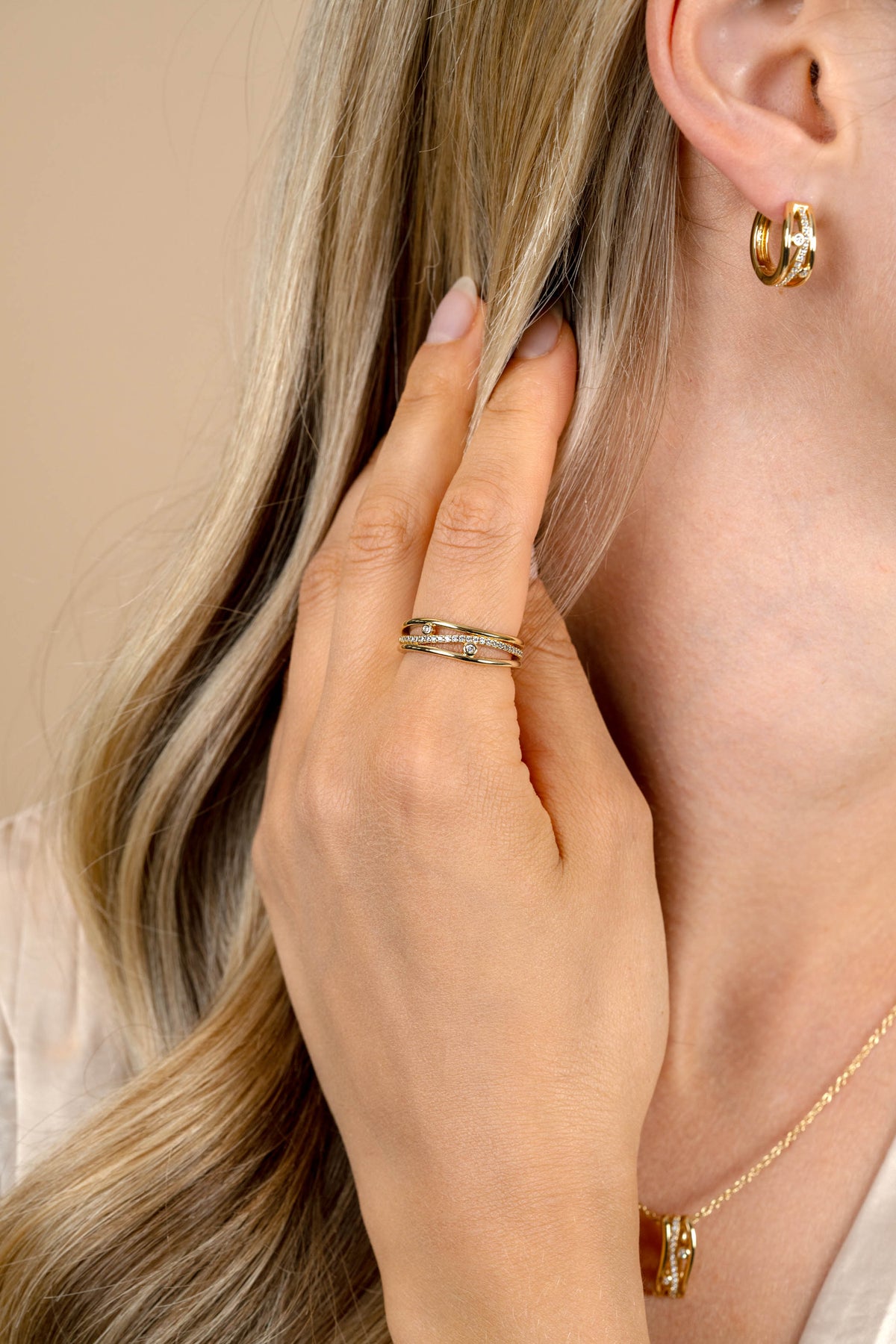 Een blonde vrouw toucheert haar haar bij haar oor, accentueert gouden oorbellen, een delicate gouden ketting en de Zinzi Ring Zilver ZIR2685 van Zinzi.