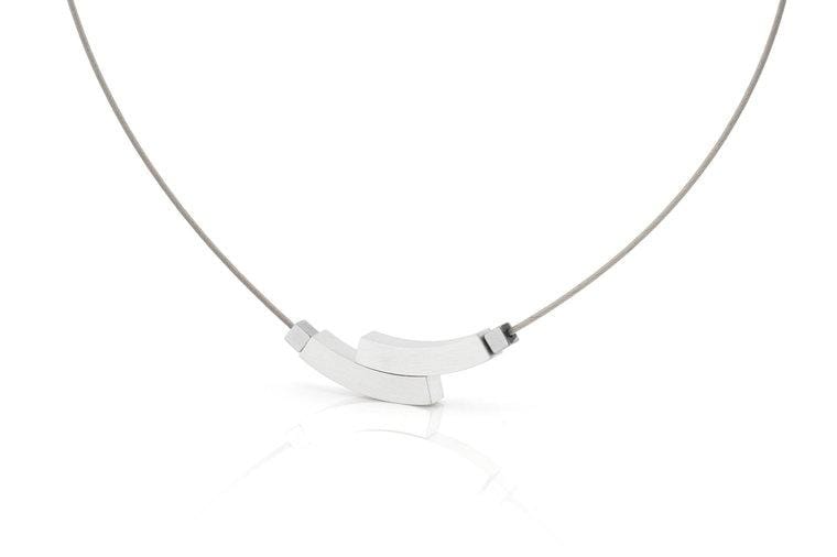 De Collier Dubbele boog C208 van CLIC Creations is een minimalistische zilveren ketting met een dunne draad en twee in elkaar grijpende, gebogen zilveren staven in het midden. Het heeft een magnetische sluiting en benadrukt een uniek ontwerp van moderne elegantie, weergegeven op een witte achtergrond.