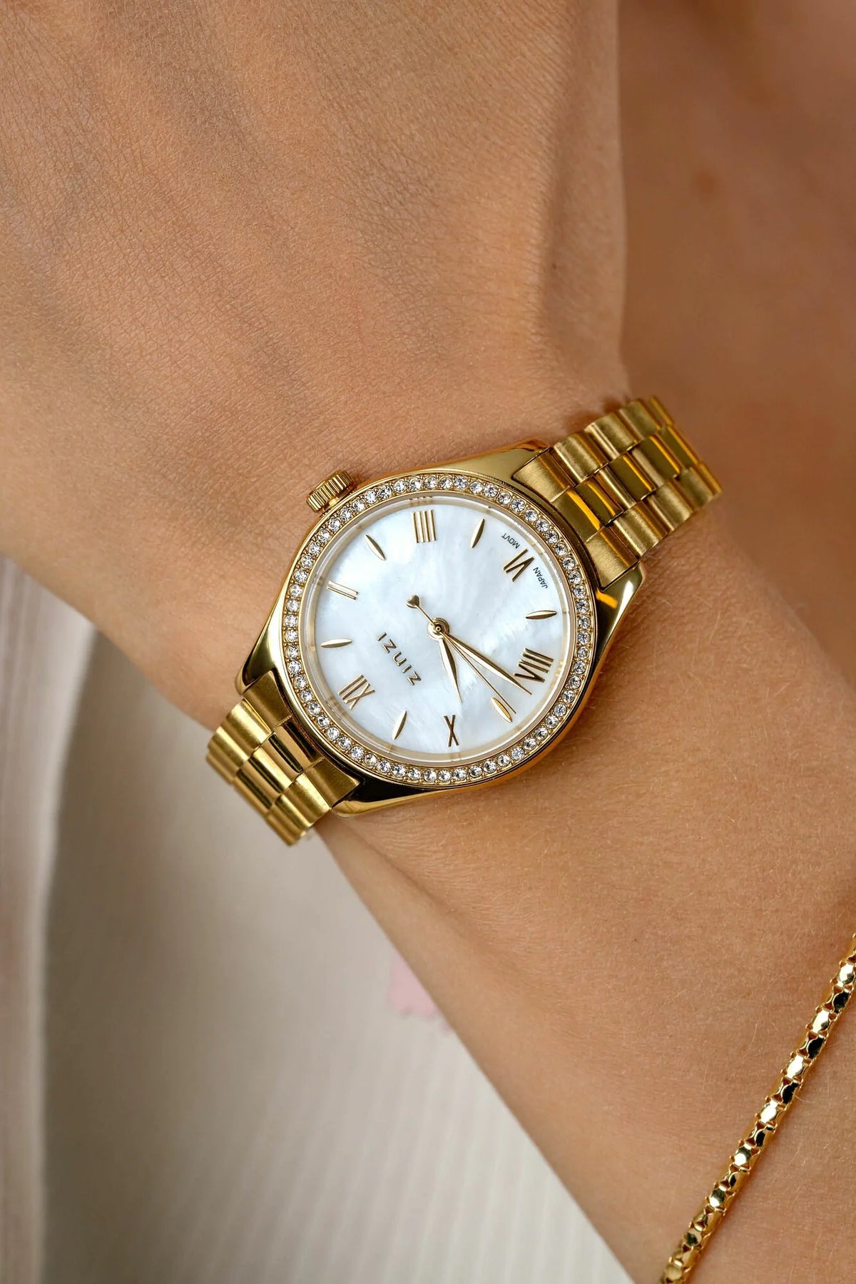 Het Zinzi Goudkleurig Horloge Staal ZIW2434 is een elegant dameshorloge met parelmoer wijzerplaat, Romeinse cijfers, een bezel met zirkonia's en wordt gedragen naast een lichtgouden schakelarmband.