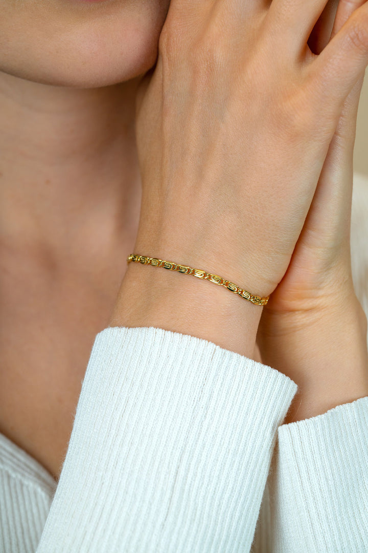 Een close-up toont een pols versierd met de Zinzi Armband verguld ZIA2712G, de kleine ovale schakels en vergulde afwerking van Zinzi complementeren een witte bovenkant met textuur terwijl de hand zachtjes rust in de buurt van het gezicht.