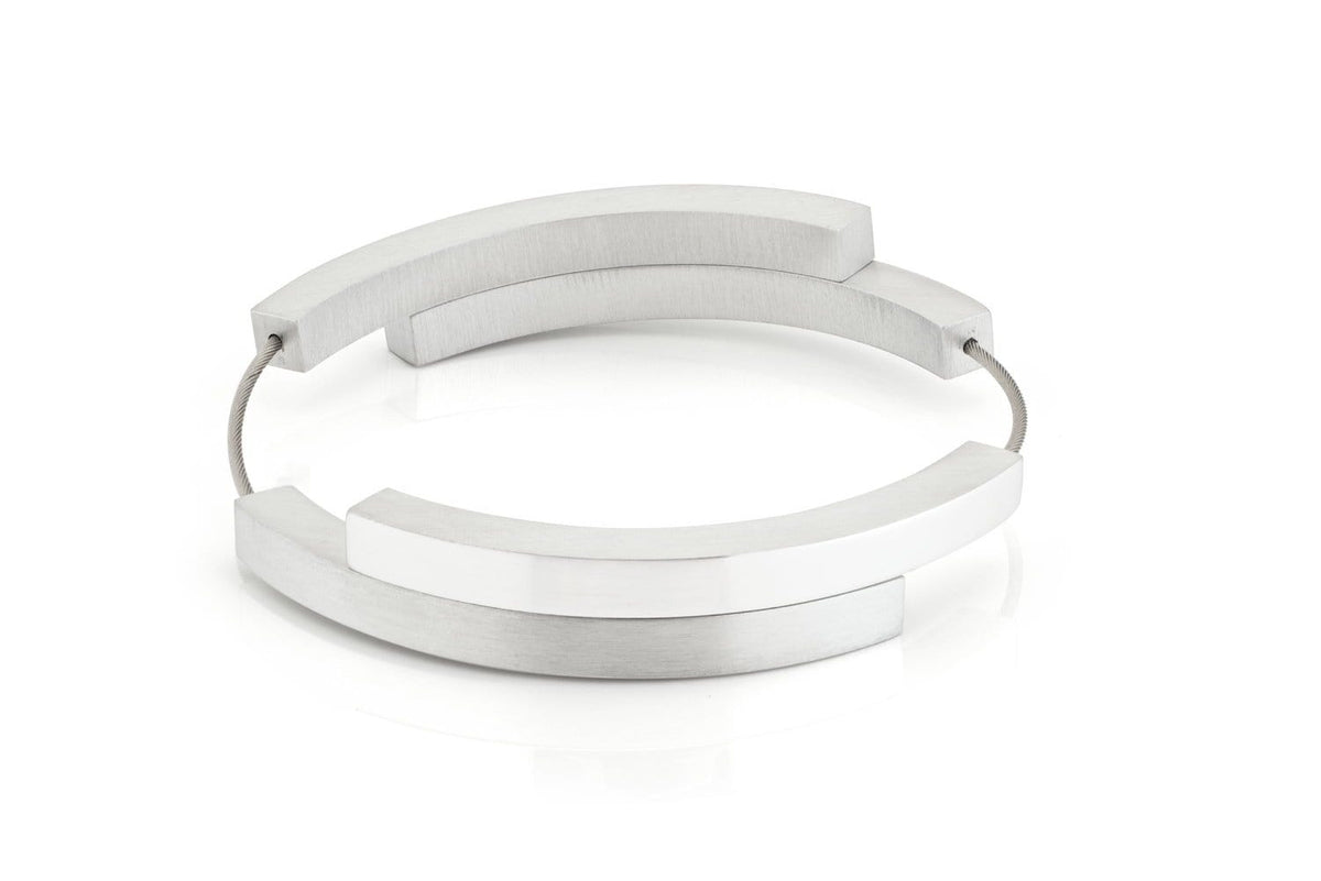 De Armband Vier bogen mat|glans A32 van CLIC Creations is een moderne, minimalistische armband met overlappende zilveren bogen die met elkaar verbonden zijn door een dunne draad en heeft een magnetische sluiting. Dit geometrische stuk is handgemaakt in Nederland en wordt tentoongesteld tegen een effen witte achtergrond.