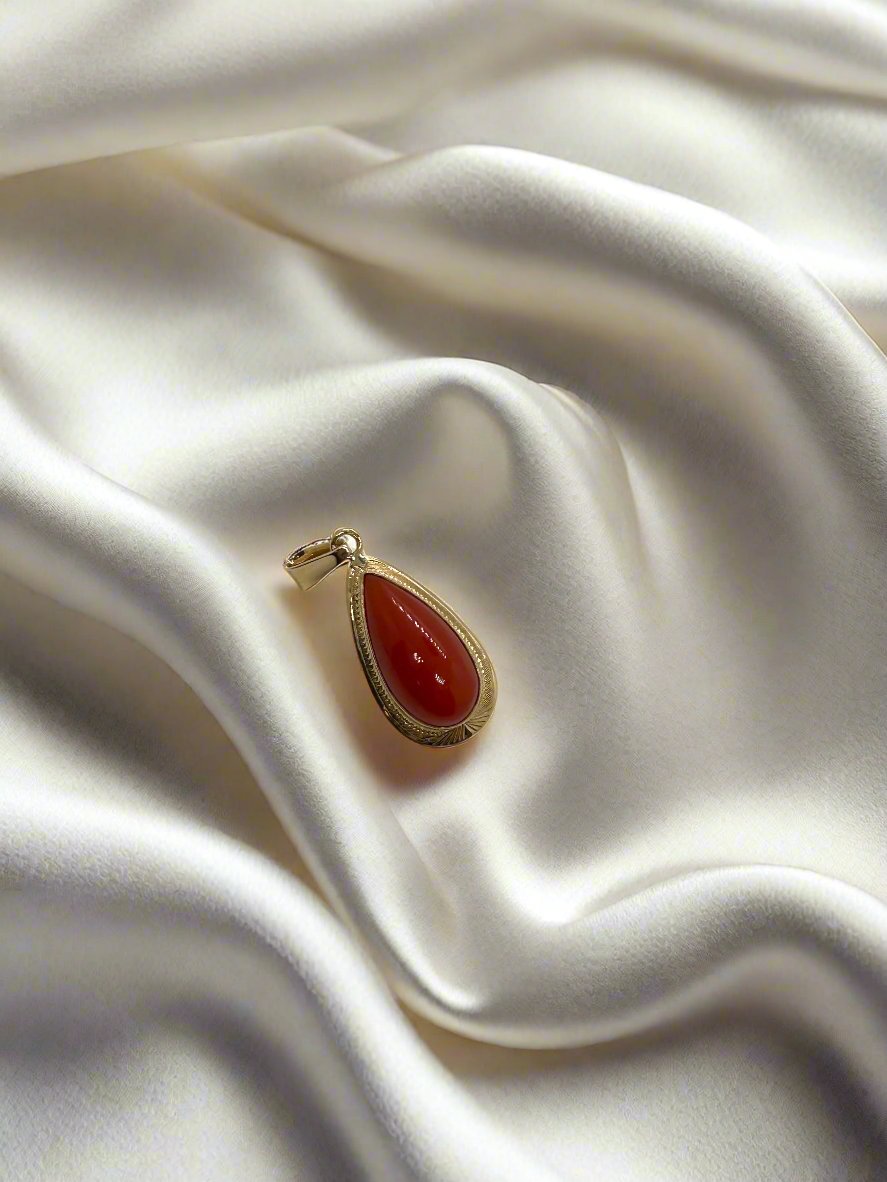 Vintage gouden hanger met 14k bloedkoraal in druppelvorm op een satijnen ondergrond.