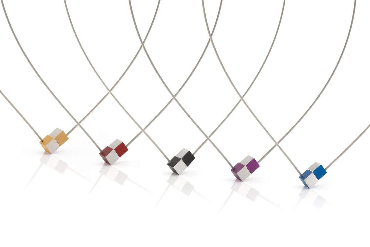 De Collier Twee kubusjes Oranje Paars met gouden draad CG205OP van CLIC Creations is een modern kunstwerk dat met de hand in Nederland is gemaakt. Het bestaat uit vijf dunne, gebogen draden met kleine geometrische vormen in levendig oranje, rood, zwart, paars en blauw tegen een witte achtergrond en is een echte blikvanger in elke ruimte.
