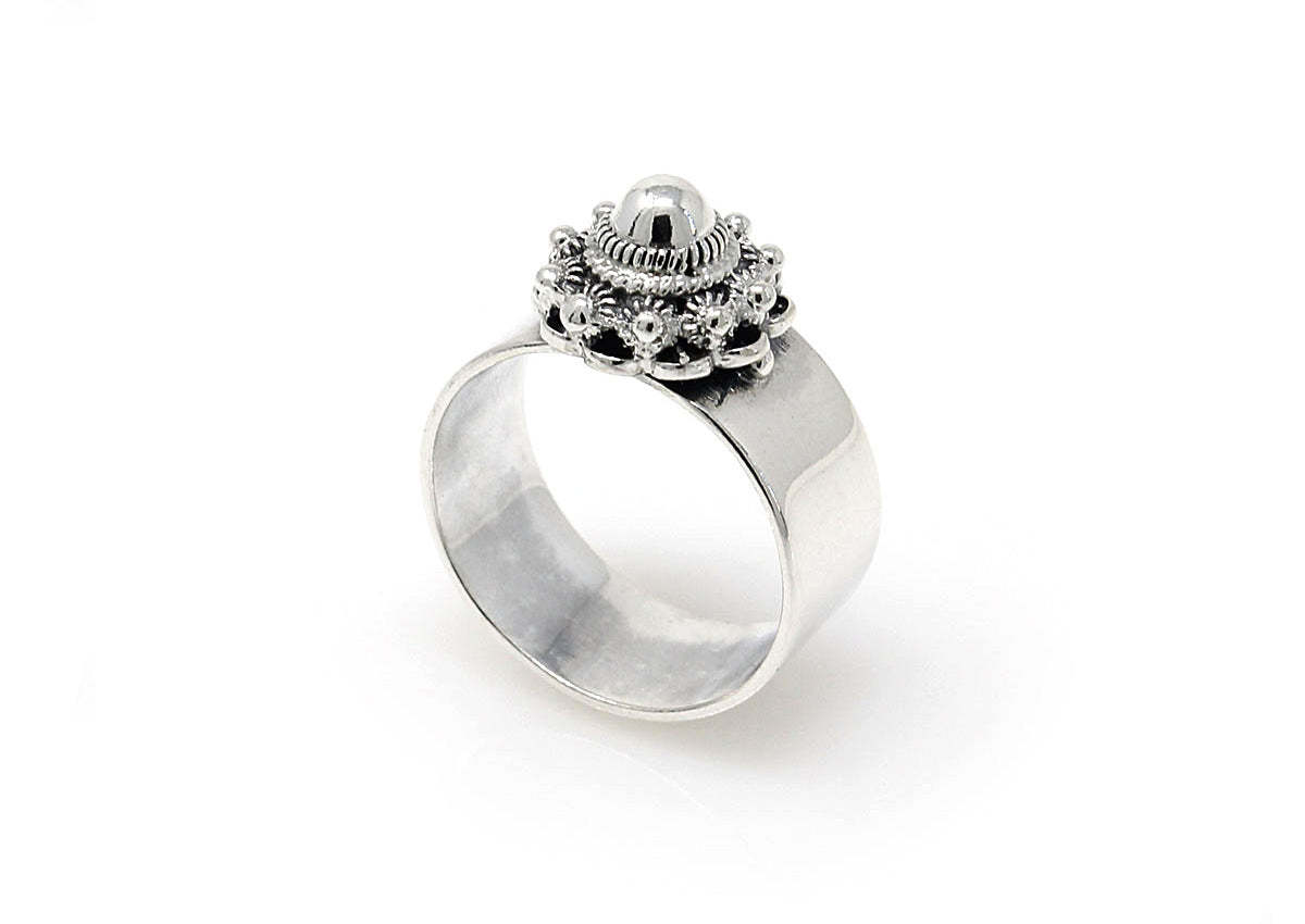 De Zeeuwse Knoop Ring Zilver nr12 van Dutch Button is een zilveren ring met een sierlijk ontwerp en een bolvormig middenstuk omringd door ingewikkelde versieringen. Het heeft een brede, gladde band die de gedetailleerde bovenkant benadrukt en is rechtop geplaatst op een witte achtergrond.