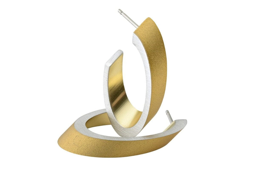Ovale creolen Goud|Geel O21G van CLIC Creations hebben een modern gedraaid ontwerp in goud en zilver, gepresenteerd op een witte achtergrond. Gemaakt van chirurgisch edelstaal, hebben deze oorbellen een matte afwerking voor een strakke, elegante look en zijn hypoallergeen.