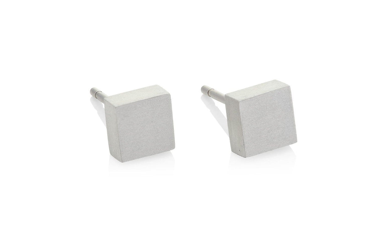 De CLIC Creations Oorsteker Klein vierkant O37 zijn minimalistische vierkante oorstekers, handgemaakt en hypo-allergeen, met een matte metalen afwerking. Deze eenvoudige, geometrische oorknopjes rusten elegant op een reflecterend wit oppervlak.