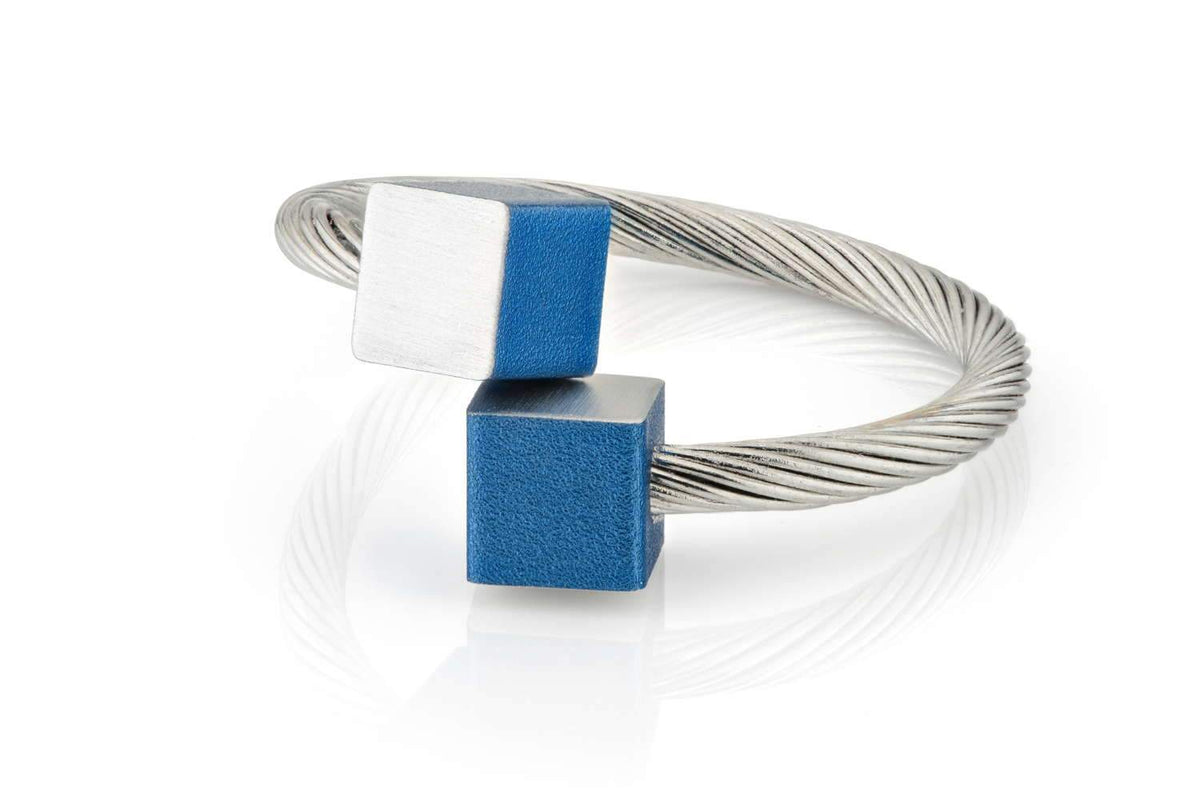 Ring met twee kubusjes, één blauw en één zilverkleurig, op een gevlochten zilveren band.
