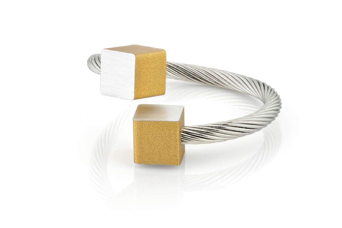 Goudkleurige ring met twee kubusjes, één in geel en één in zilver, op een gevlochten metalen band.