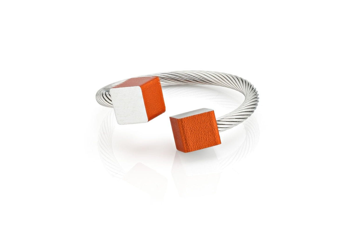 De Ring Kubusjes Oranje R4O van CLIC Creations is een zilveren gedraaide kabelarmband met twee kubusuiteinden: een half zilver, half oranje en de andere helemaal oranje. Het open-top design combineert op unieke wijze eigentijdse stijl met minimalistische flair.