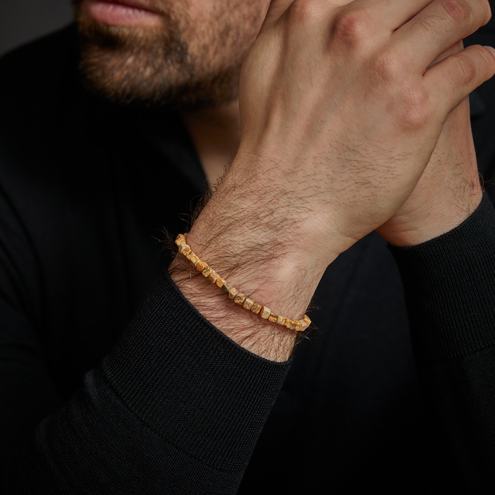 Een bebaarde man in een zwart shirt met lange mouwen omklemt zijn handen en laat de Rebel & Rose "Roll The Dice - Woodstock - 4mm" heren kralen armband om zijn pols zien. Zijn gezicht is gedeeltelijk zichtbaar, met een baard en snor.