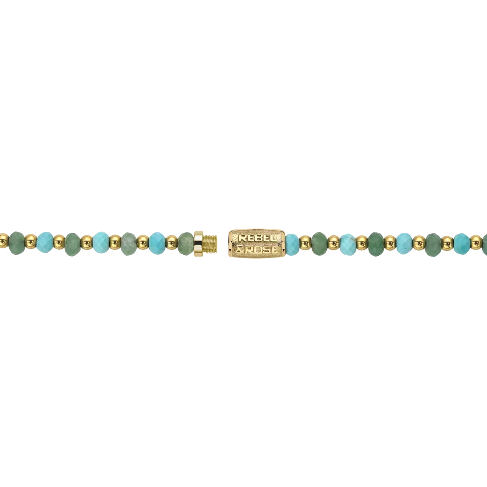 De ketting Blue Green Adventure - 4mm van Rebel & Rose heeft gouden en turquoise kralen met een 18kt vergulde rechthoekige sluiting met de gravure "Rebel Noise," op een zwarte achtergrond.