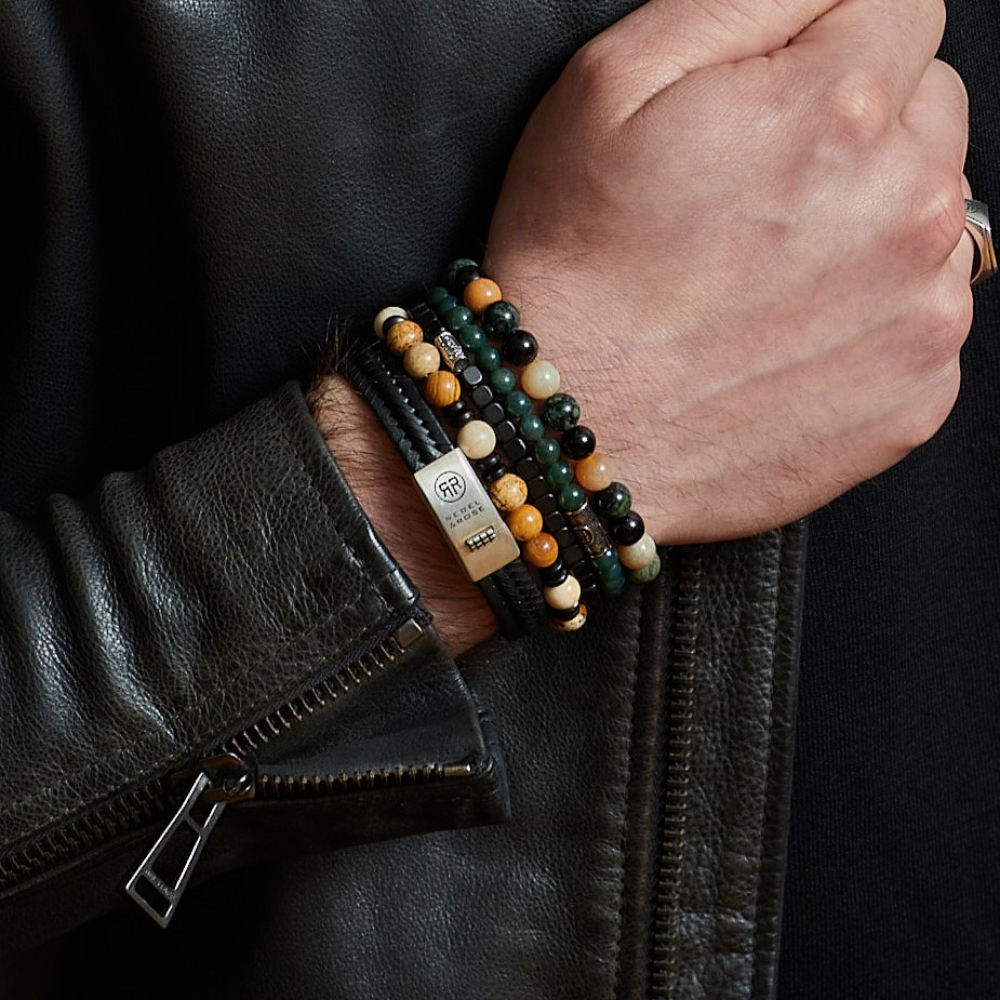 Een persoon met een zwarte leren jas en gouden ring toont zijn pols versierd met kleurrijke kralenarmbanden, waaronder de Rebel & Rose Autumn Storm - 8mm - Kralen Heren Armband en andere Rebel & Rose stukken, plus een metalen accent.