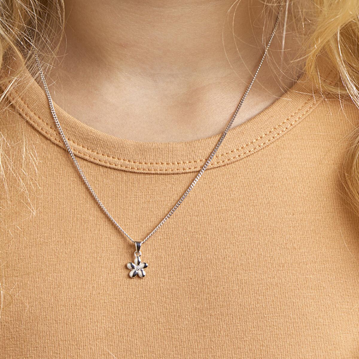 Een persoon draagt een lichtbruine top en een Van der Kooij Collectie collier bloem 1,1 mm 36 + 4 cm zilver gerhodineerd. Het collier met een delicate bloemenhanger en kleine zirkonia hanger staat centraal, afgebeeld op de bovenborst.