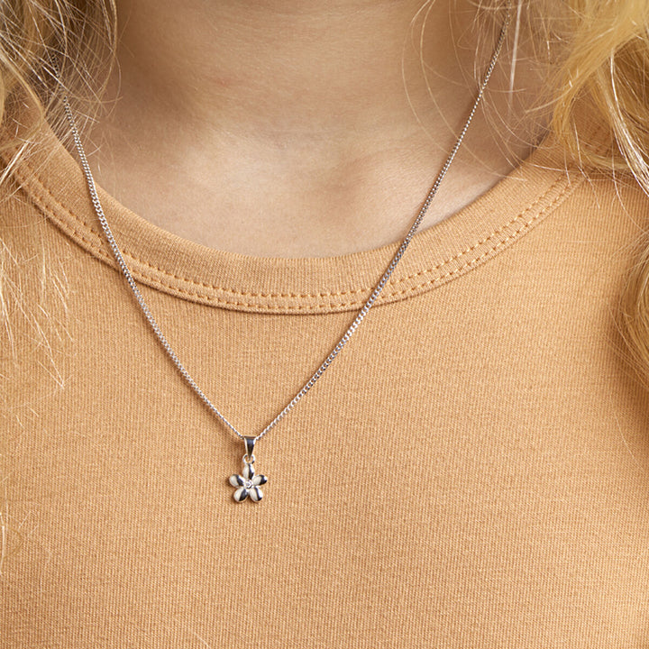 Een persoon draagt een lichtbruine top en een Van der Kooij Collectie collier bloem 1,1 mm 36 + 4 cm zilver gerhodineerd. Het collier met een delicate bloemenhanger en kleine zirkonia hanger staat centraal, afgebeeld op de bovenborst.