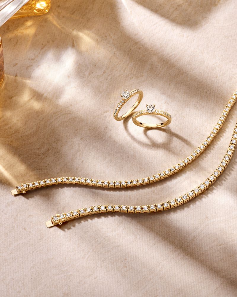 Twee Geelgouden Tennisarmbanden met Briljanten van Excellent Jewelry (14 karaat goud, 2.00 karaat diamant) schitteren op beige marmer in natuurlijk licht, omringd door gouden ringen met heldere briljanten.