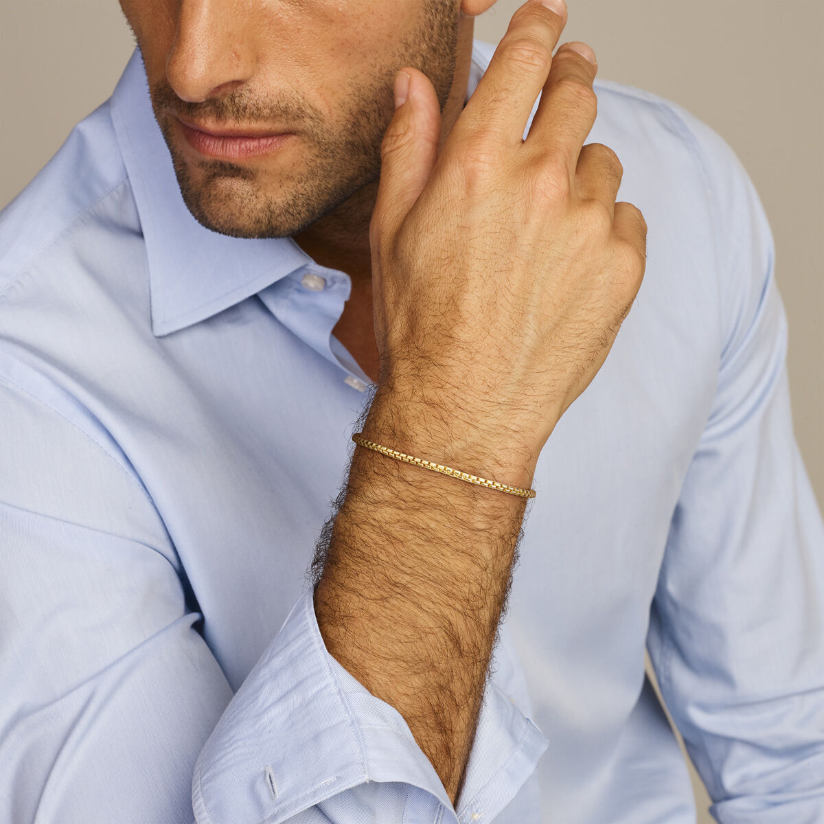 Een man in een lichtblauw overhemd laat zijn kin op zijn hand rusten en toont de Van der Kooij Collectie Gouden armband heren venetiaans bol 2,5 mm 14K om zijn pols.