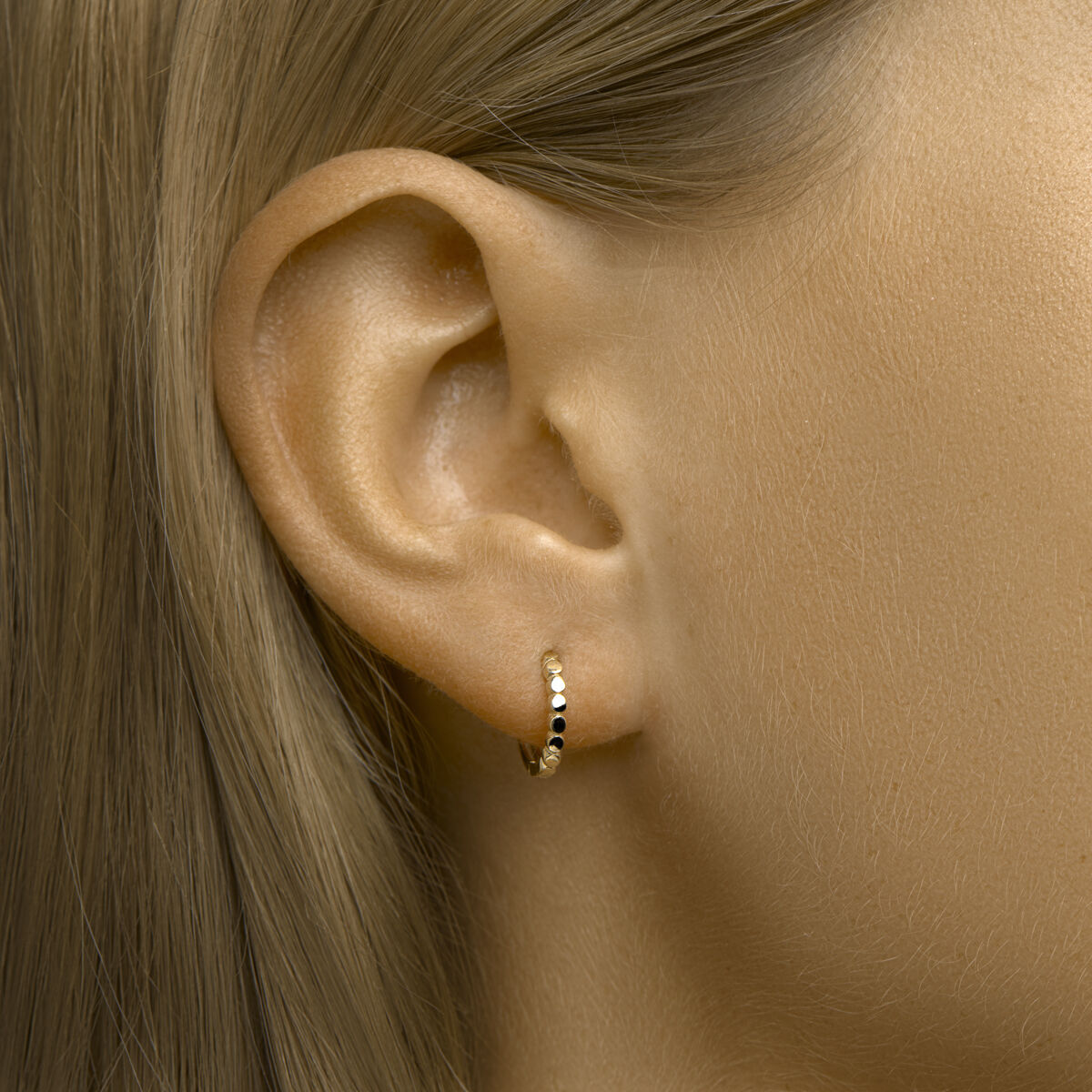 Close-up van het oor van een vrouw met Van der Kooij Collectie klapoorbellen 14K geelgoud met zwarte en gouden kraaltjes. Haar steile blonde haar is weggestopt achter haar oor, tegen een neutrale achtergrond.