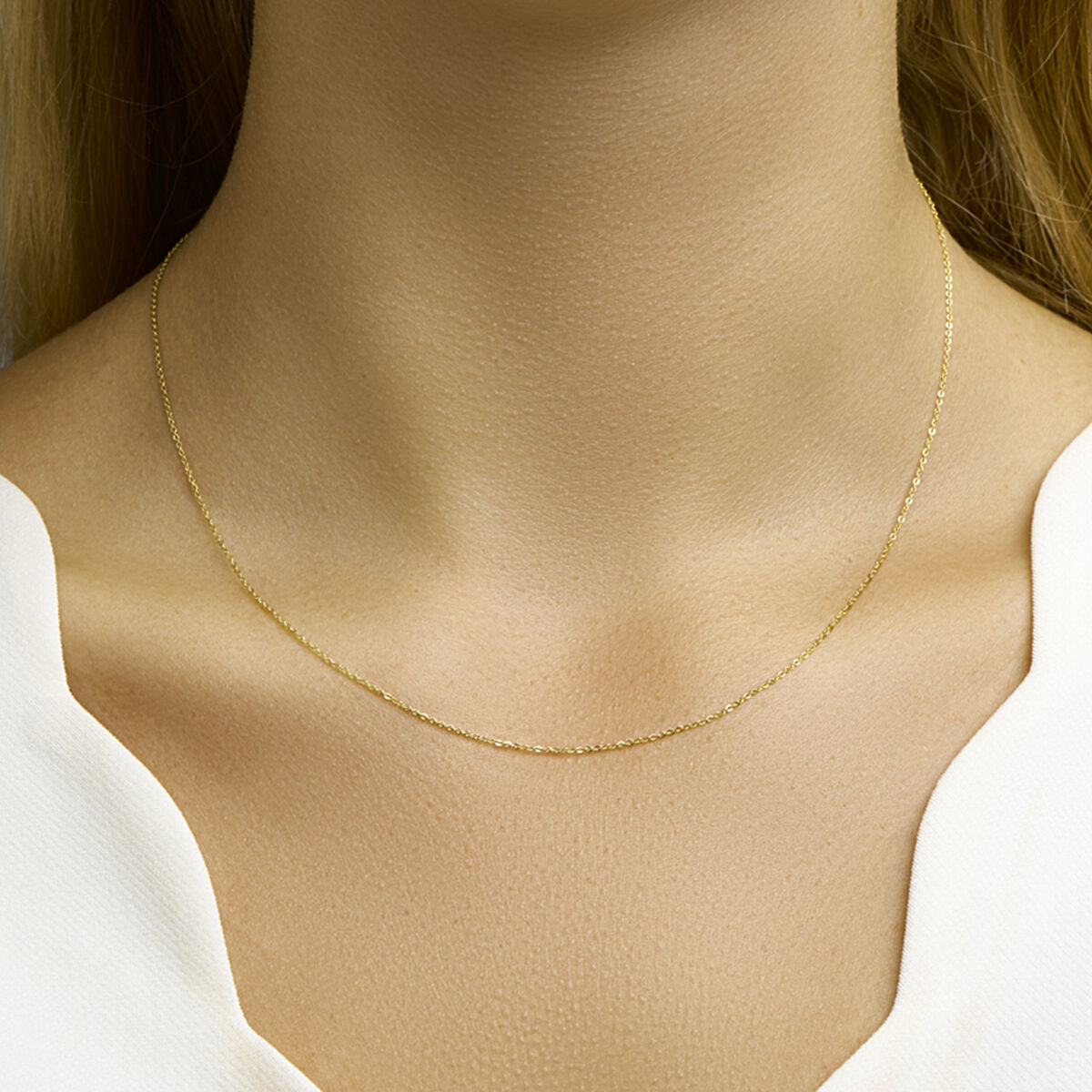 Een close-up van de hals van een vrouw met de Van der Kooij Collectie collier anker plat 1,0 mm 14K geelgoud met een witte v-hals top. Deze unisex ketting brengt tijdloze elegantie in elke look.