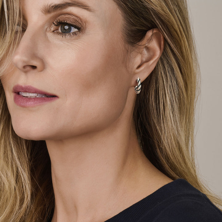 Een vrouw met lang blond haar en natuurlijke make-up, in een donker topje, kijkt iets opzij. In haar linkeroor draagt ze Van der Kooij Collectie oorringen gedraaid donkergroen emaille zilver gerhodineerd tegen een neutrale achtergrond.