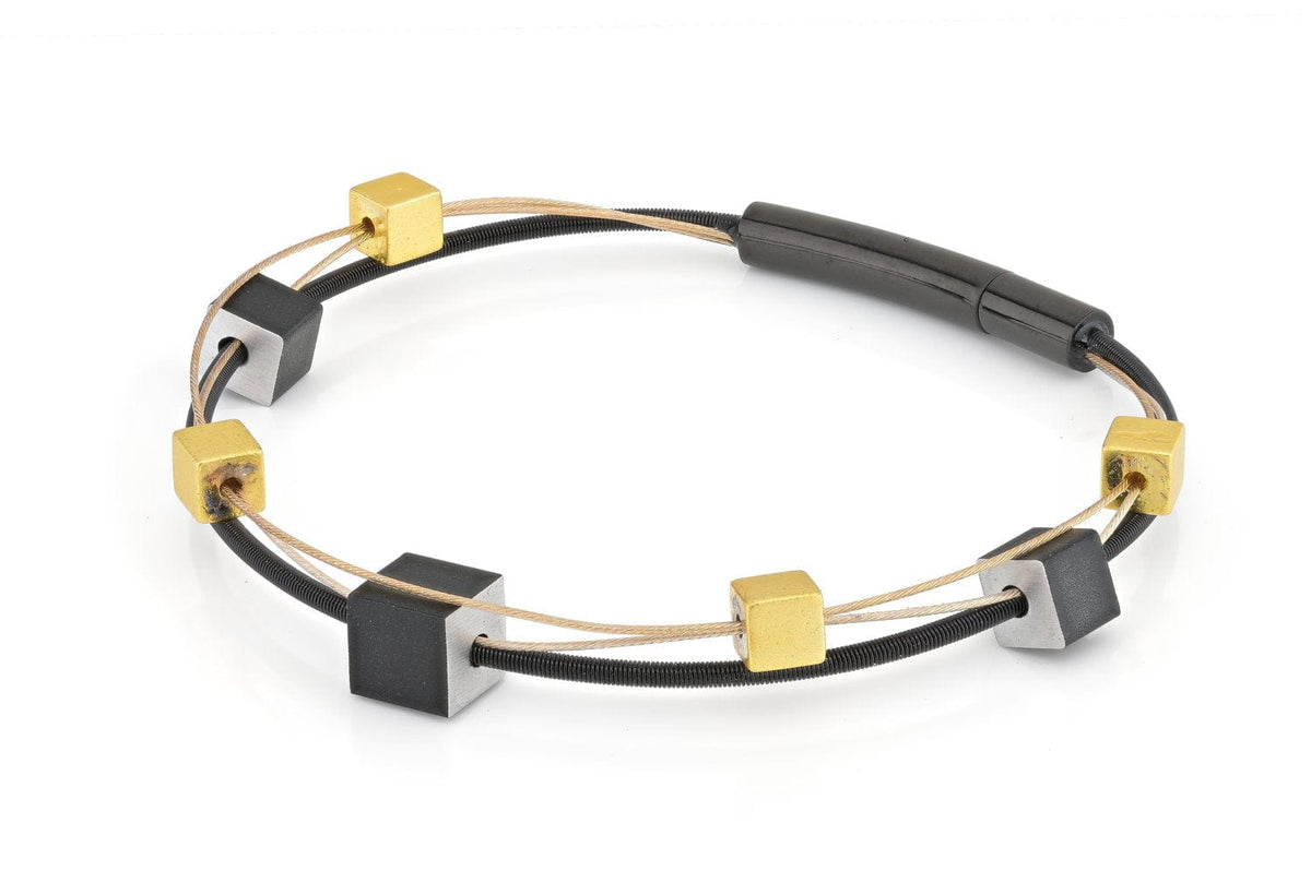 De Armband speelse kubusjes goud|zwart A257Z van CLIC Creations toont handgemaakte afwisselend gouden en zwarte kubuskralen op twee dunne koorden met een strakke cilindrische bajonetsluiting voor eenvoudig dragen.