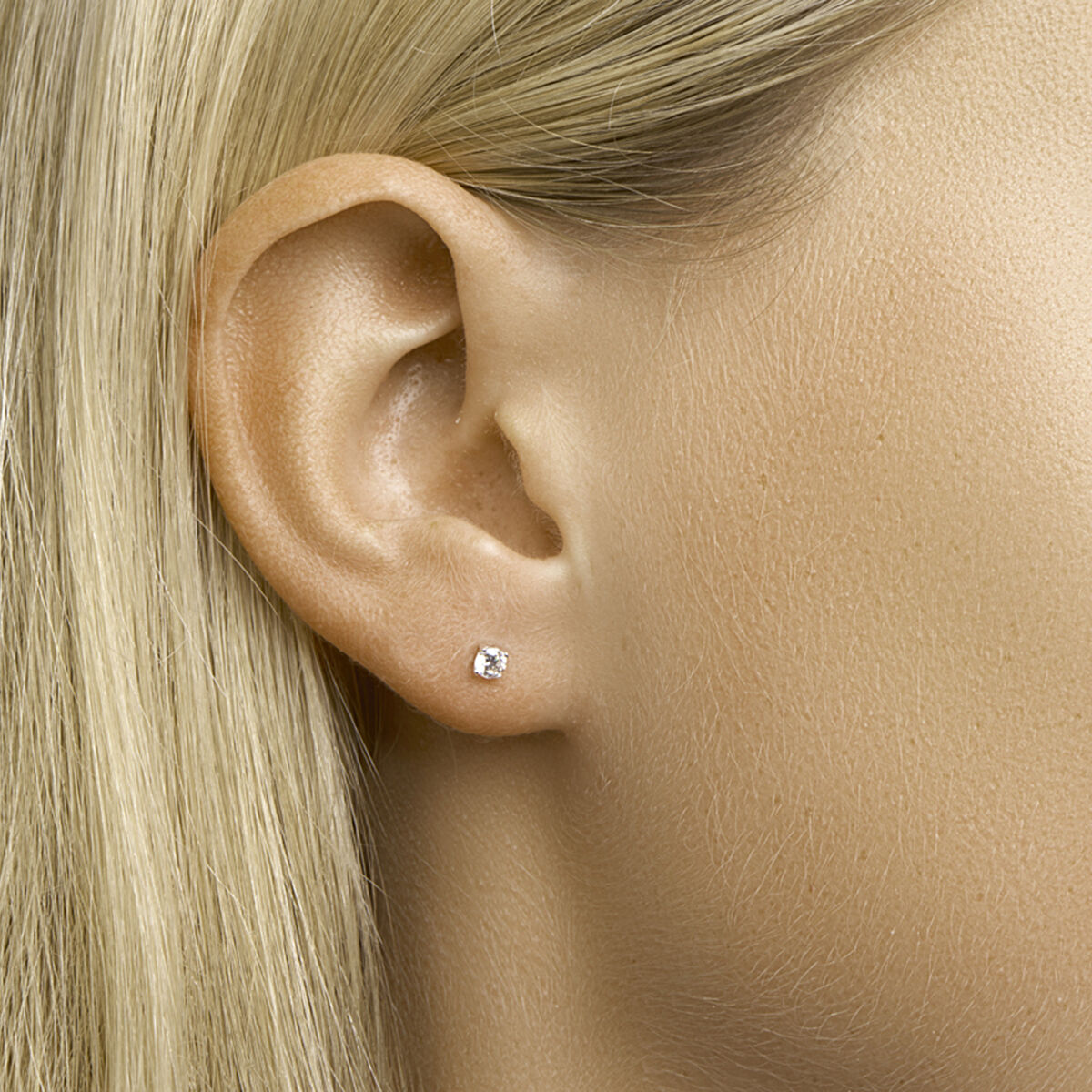 Close-up van iemands oor met steil blond haar, met Van der Kooij Collectie oorknoppen zirkonia zilver wit. De gladde huid en de fonkelende knop benadrukken de verfijnde elegantie van dit sieraad.