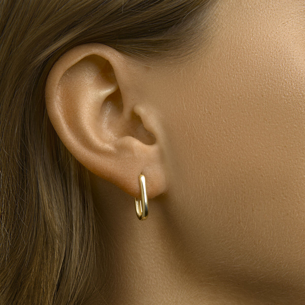 Close-up van een vrouwenoor met Van der Kooij Collectie klapoorringen paperclip 1 micron zilver verguld (geel); ze heeft een lichte huid en steil, lichtbruin haar tegen een neutrale, onscherpe achtergrond.