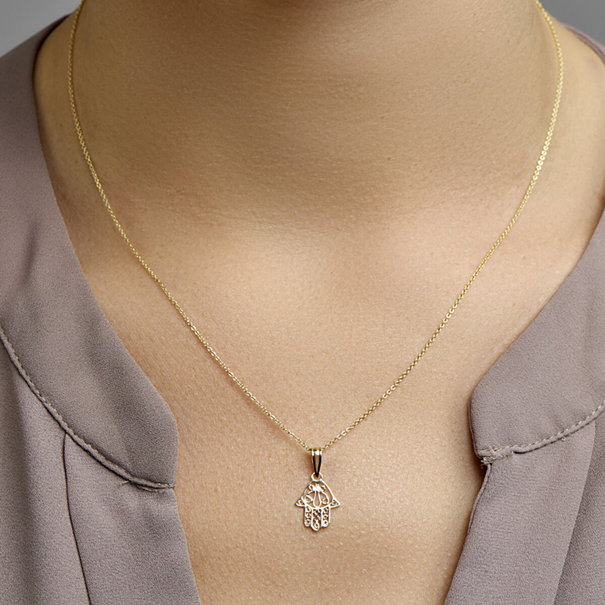 Een close-up van een persoon die de Van der Kooij Collectie hanger Fatima hand 14K geelgoud draagt, tegen een lichte huid en een taupe blouse met V-hals.