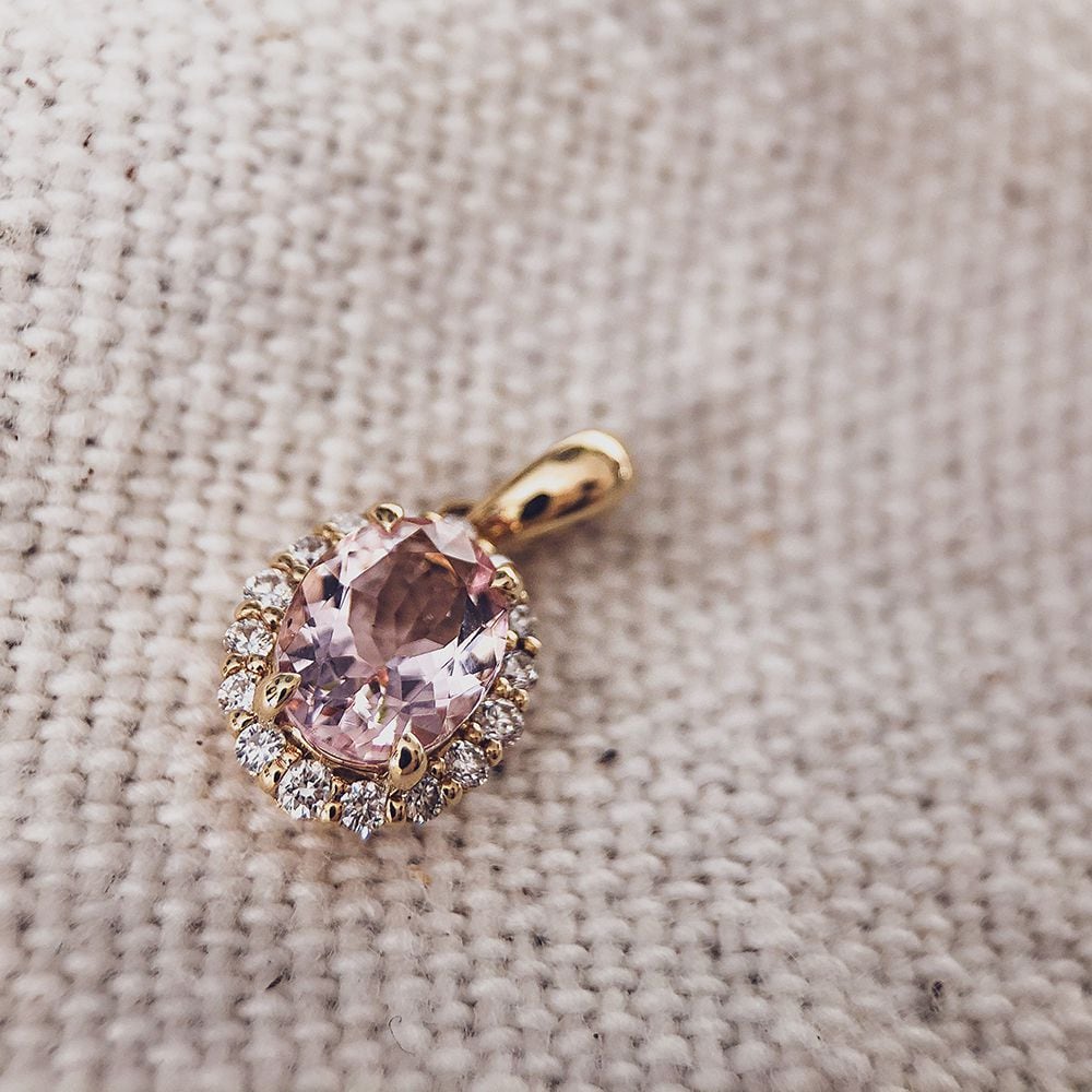 De Hanger geelgoud morganiet+briljant van Excellent Jewelry heeft een grote ovale morganiet edelsteen met briljant accenten, prachtig weergegeven op een beige gestructureerd oppervlak.