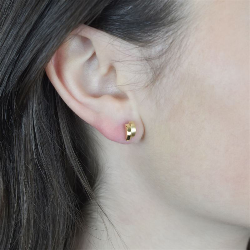 Close-up van een persoon met steil bruin haar en een lichte huid die Boccia Titanium Oorstekers gp NL 0552-05-elegante, goudkleurige oorbellen met dubbele lus van Boccia draagt, uitgelicht tegen een onscherpe achtergrond.