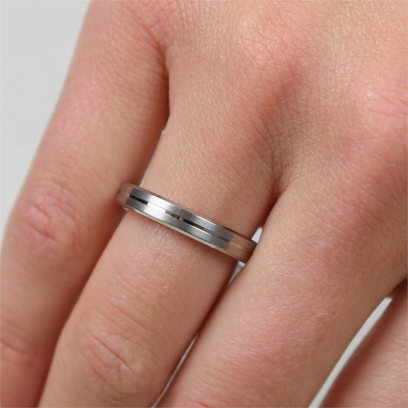 Een close-up van een hand met de Boccia Titanium Ring 0148-01: een strakke, zilverkleurige band met een subtiele groef in het midden van Boccia, die elegant op de ringvinger wordt gepresenteerd.