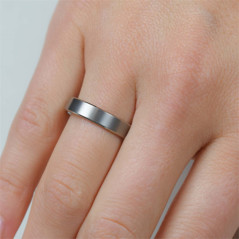 Een hand met een eenvoudige, gladde Boccia Titanium Ring 0121-03 siert de ringvinger tegen een effen achtergrond, waardoor dit harsaccessoire in mat titanium een ingetogen elegantie uitstraalt.