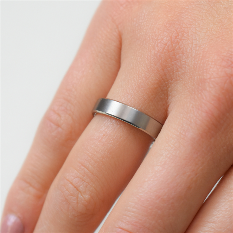Een close-up van een hand met de Boccia Titanium Ring 0120-03 van Boccia. Dit is een eenvoudige, gladde zilveren titanium ring. Deze ring is aan de ringvinger bevestigd tegen een neutrale achtergrond.
