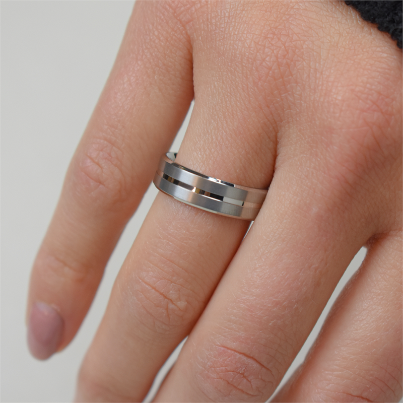 Een close-up toont een hand met de Boccia Titanium Ring 0101-07, een ring met dubbele band van Boccia aan de middelvinger. De ring heeft een lichte achtergrond met een donkere huls en wordt geleverd in een geschenkdoosje. Perfect om cadeau te geven.
