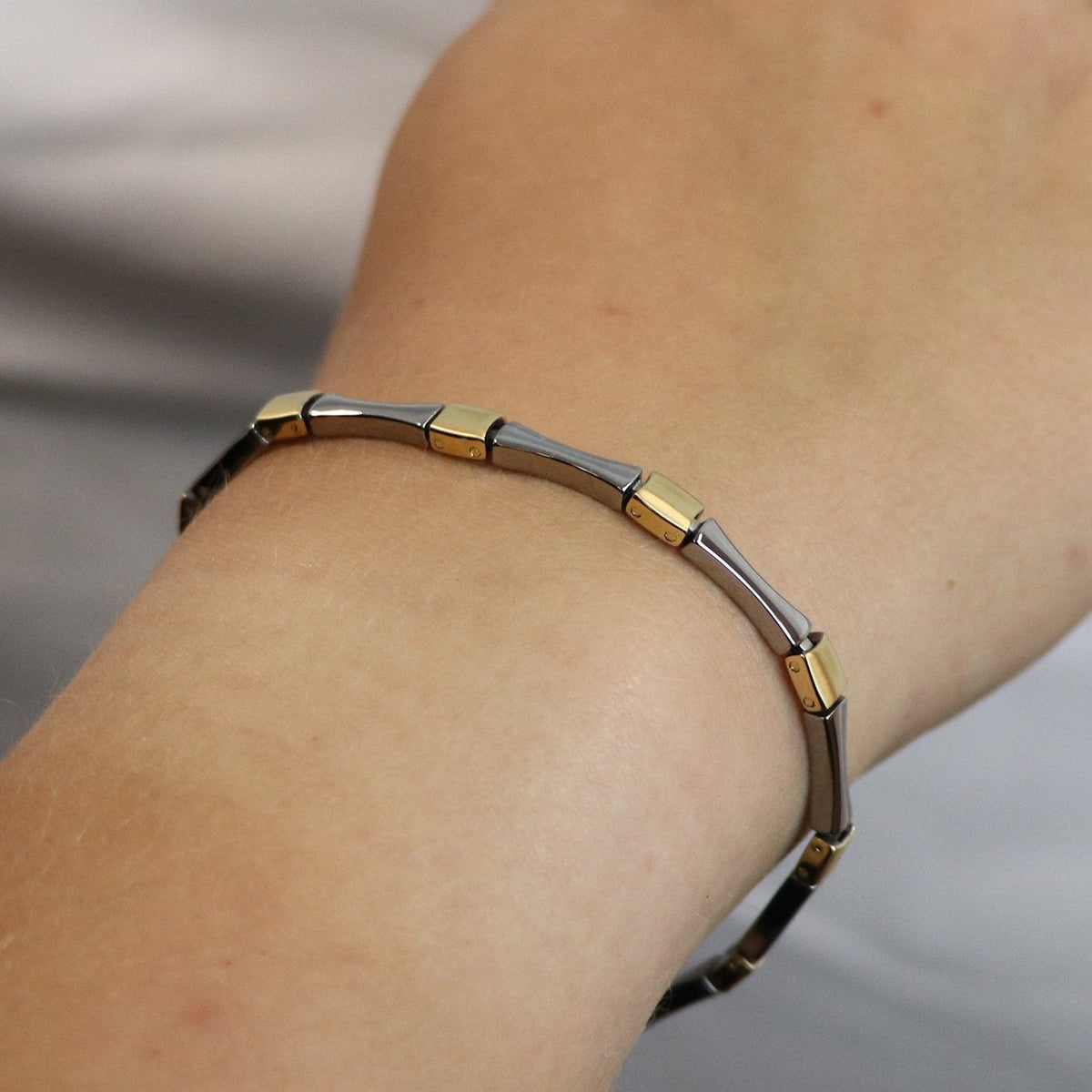 Een close-up van een pols versierd met de Boccia Titanium Armband Bicolor 03037-04, met afwisselend zilveren en gouden schakels van Boccia tegen een zachte, neutrale achtergrond.