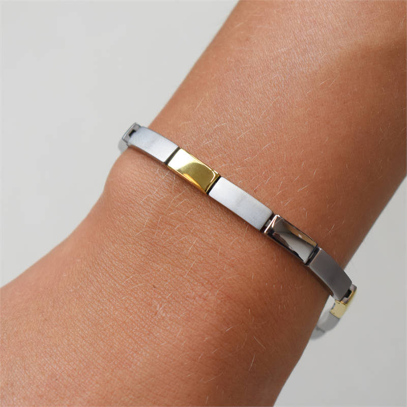 Een close-up van een pols die de Boccia Titanium Armband Bicolor 03036-02 draagt, met afwisselend zilveren en gouden rechthoekige schakels tegen een lichte achtergrond.