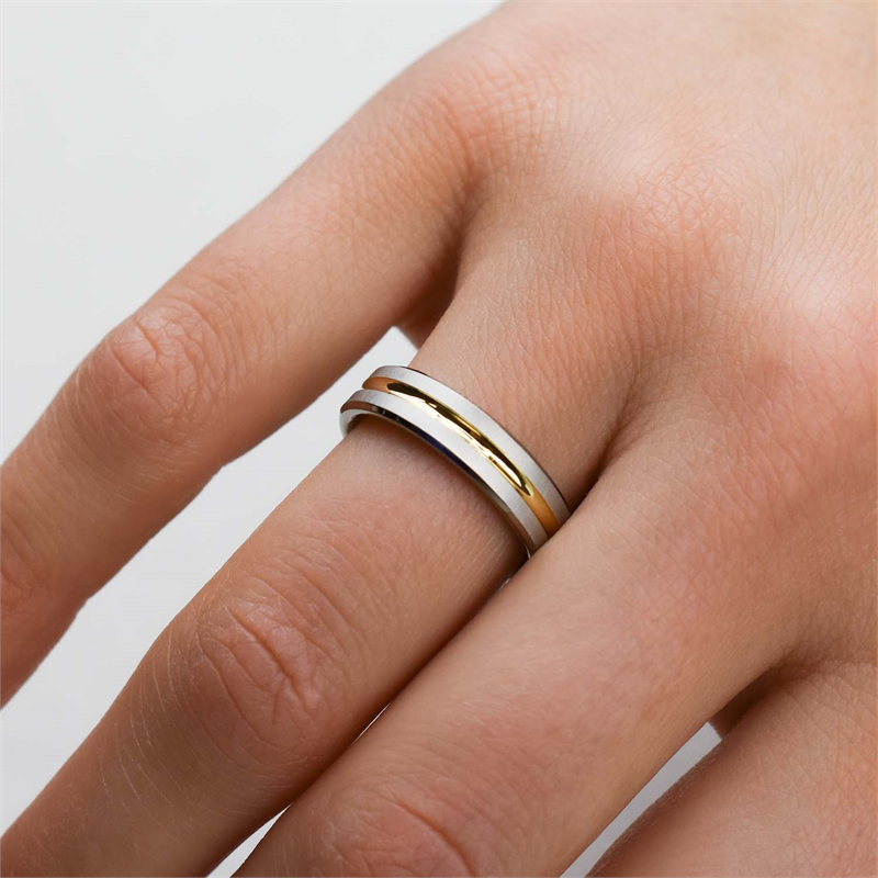 Een close-up van een hand met de Boccia Titanium Ring Bicolor 0144-02 van Boccia. De verweven zilveren en gouden banden op de ringvinger zijn te zien tegen een lichte achtergrond: een tijdloos accessoire.
