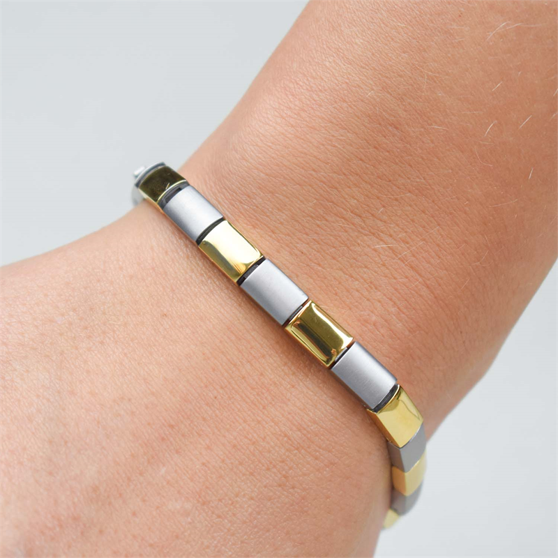 Een close-up van een pols met de Boccia Titanium Armband Bicolor 0313-02, met tweekleurige gouden en zilveren schakels. De Boccia armband zit strak en benadrukt het elegante design op een lichte huidskleur.