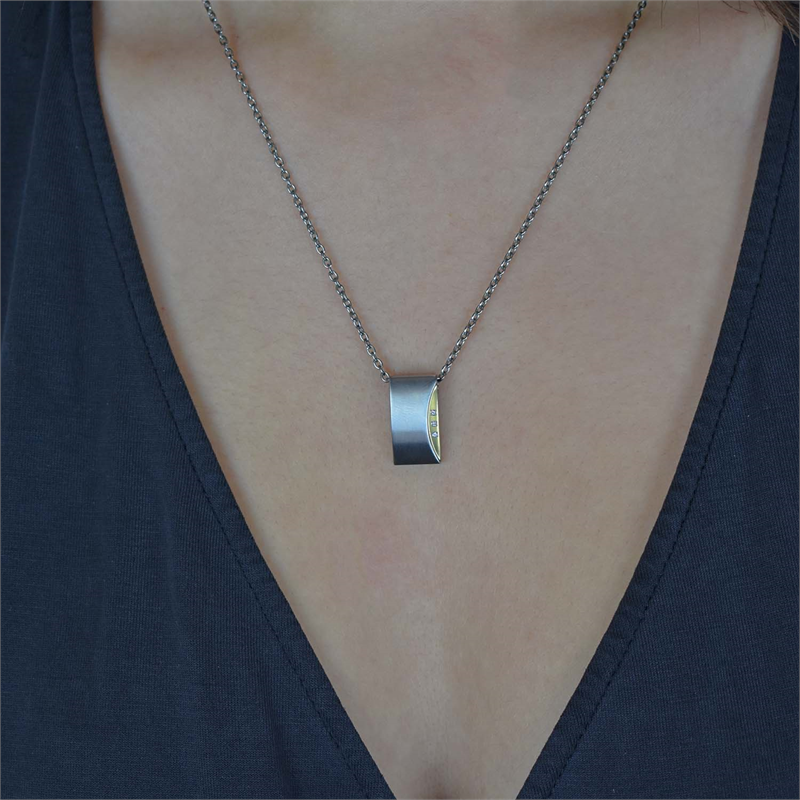 Een persoon draagt de Boccia Titanium Hanger Bicolor dia 3/0.015 - 0793-04 van Boccia, een moderne rechthoekige zilveren hanger met goudkleurige details, boven een donker shirt met diepe V-hals.