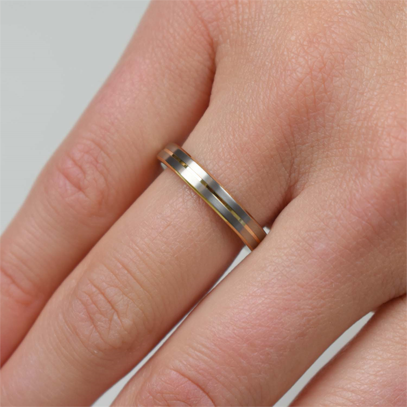 Een close-up toont een hand met de Boccia Titanium Ring Bicolor 0148-02 van Boccia, met gouden en zilveren titanium banden om de ringvinger tegen een lichte, neutrale achtergrond.