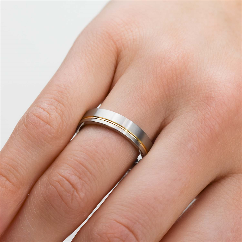 Een close-up van een hand met de Boccia Titanium Ring Bicolor 0149-03, gemaakt van titanium met een dunne gouden streep, wordt getoond op de ringvinger tegen een effen lichte achtergrond: een tijdloos Boccia-sieraad voor elke sieradencollectie.