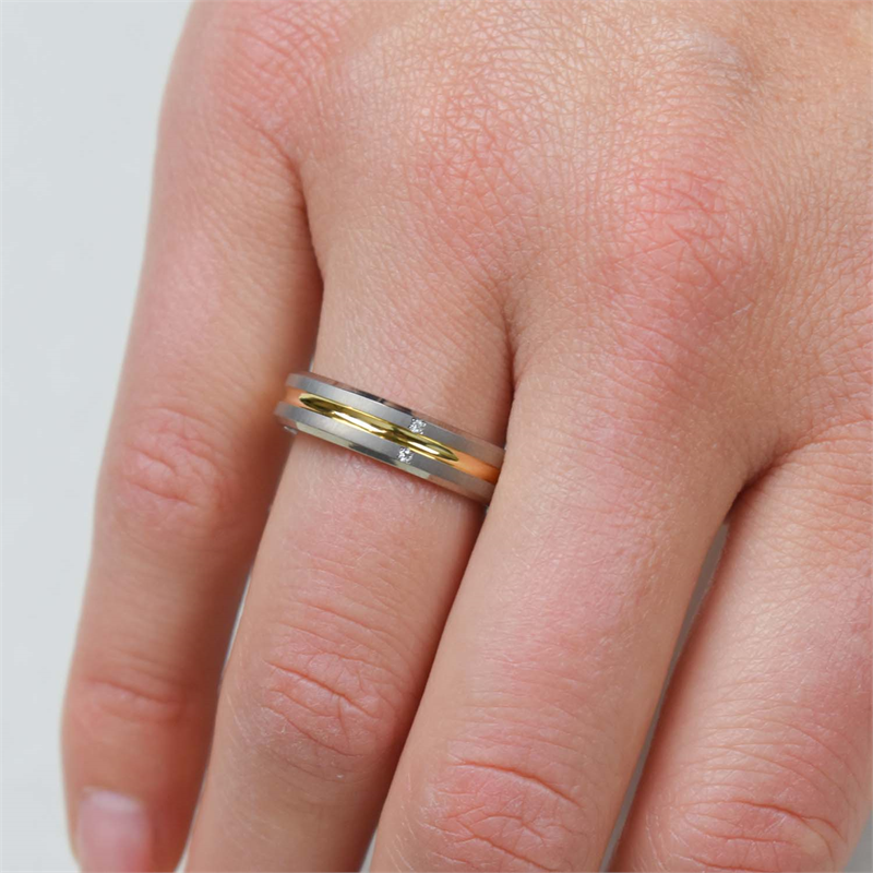 Een close-up van een hand met de Boccia Titanium Ring Bicolor dia 1/0.01 - 0144-01 van Boccia, in goud- en zilvertinten met kleine diamantaccenten, om de ringvinger tegen een lichte achtergrond.