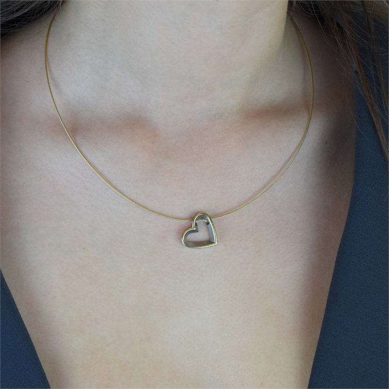 Een persoon met lang bruin haar en een donker topje met V-hals draagt een dunne gouden ketting met daarop de Boccia Titanium Hanger Bicolor dia 1/0.05 - 07014-02 van Boccia, zichtbaar vanaf de schouders tot aan de hals.