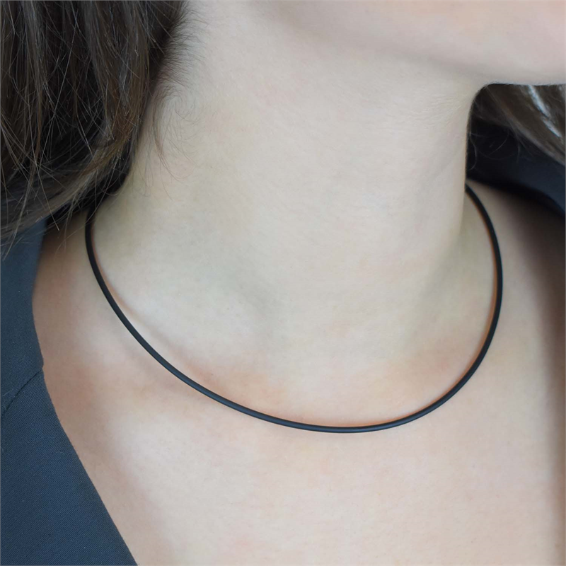 Een close-up van de nek van een vrouw die de Boccia Titanium Lengte Collier rubber 0801-01 choker van Boccia draagt, gecombineerd met een zwart topje dat bij de kraag zichtbaar is.