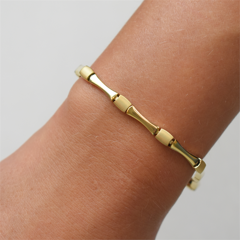 Een close-up van een pols versierd met de Boccia Titanium Armband gp 03037-03, een slanke gouden damesarmband van Boccia met een op bamboe geïnspireerd ontwerp tegen een effen, lichte achtergrond.